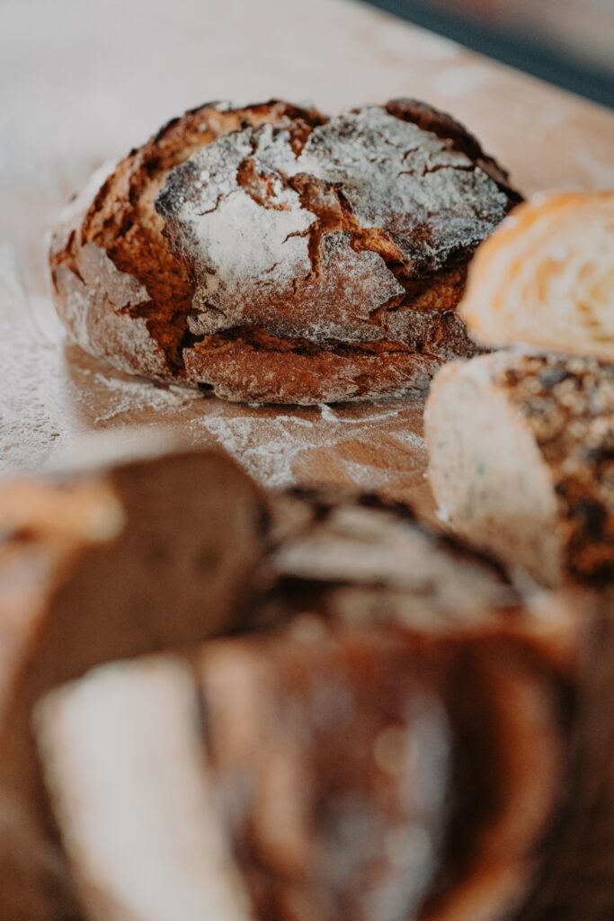 Eine Nahaufnahme von rustikalen, knusprigen Brotlaiben auf einer mit Mehl bestäubten Holzunterlage. Im Vordergrund sind einige Scheiben zu sehen, die leicht unscharf sind.